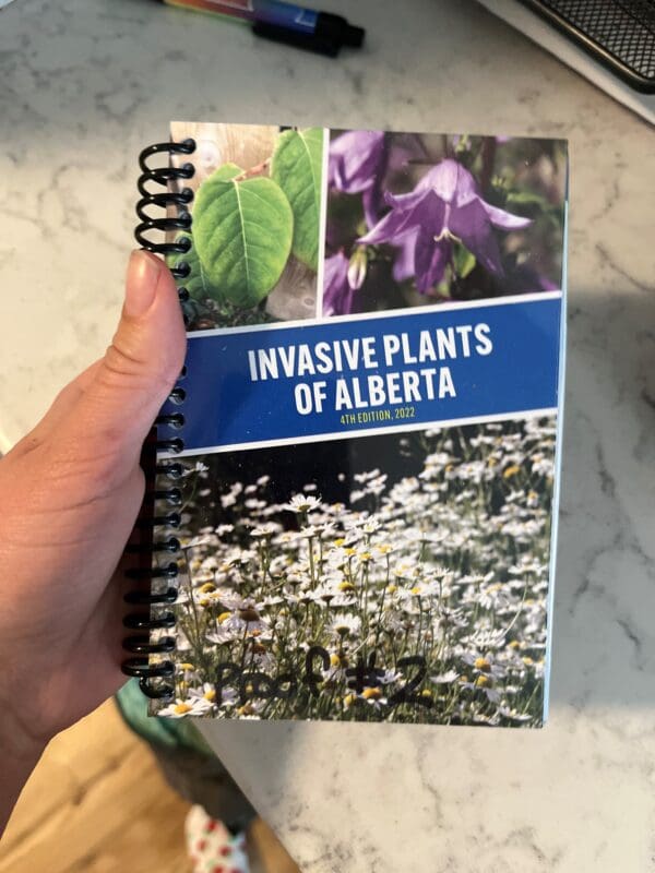 A hand holding a book with pictures of plants.
